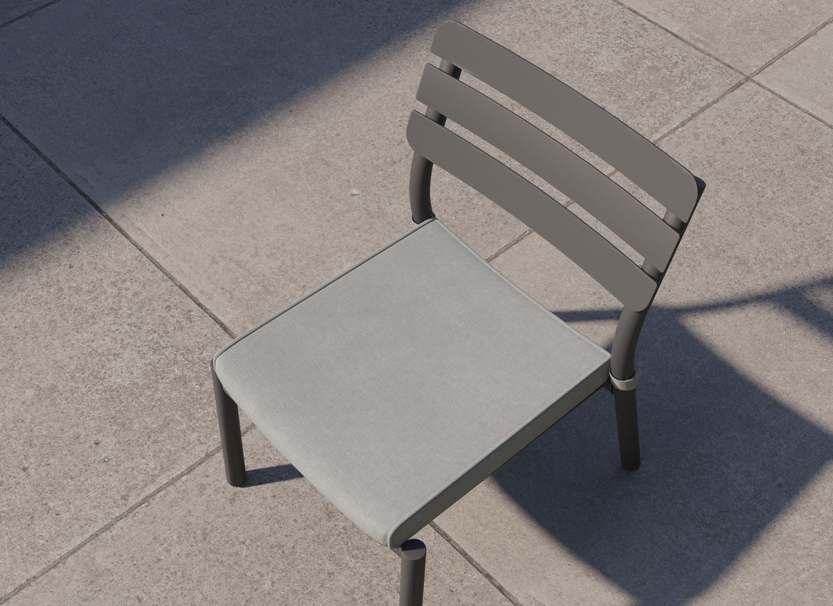 Gray armless dining chair with a sleek sintered stone seat and modern aluminum frame, set on a textured concrete surface.