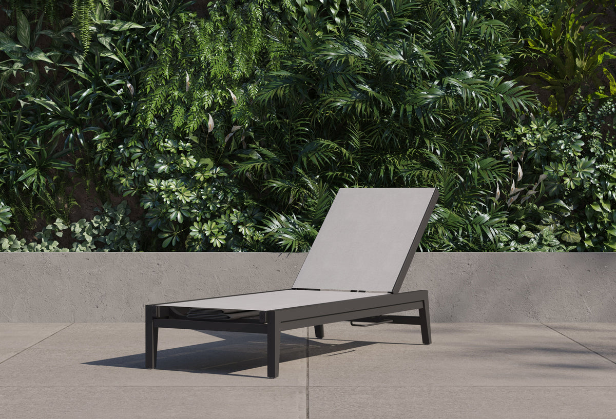 Aluminum outdoor chaise lounge with a sleek black frame and gray sling, positioned against a lush green backdrop.