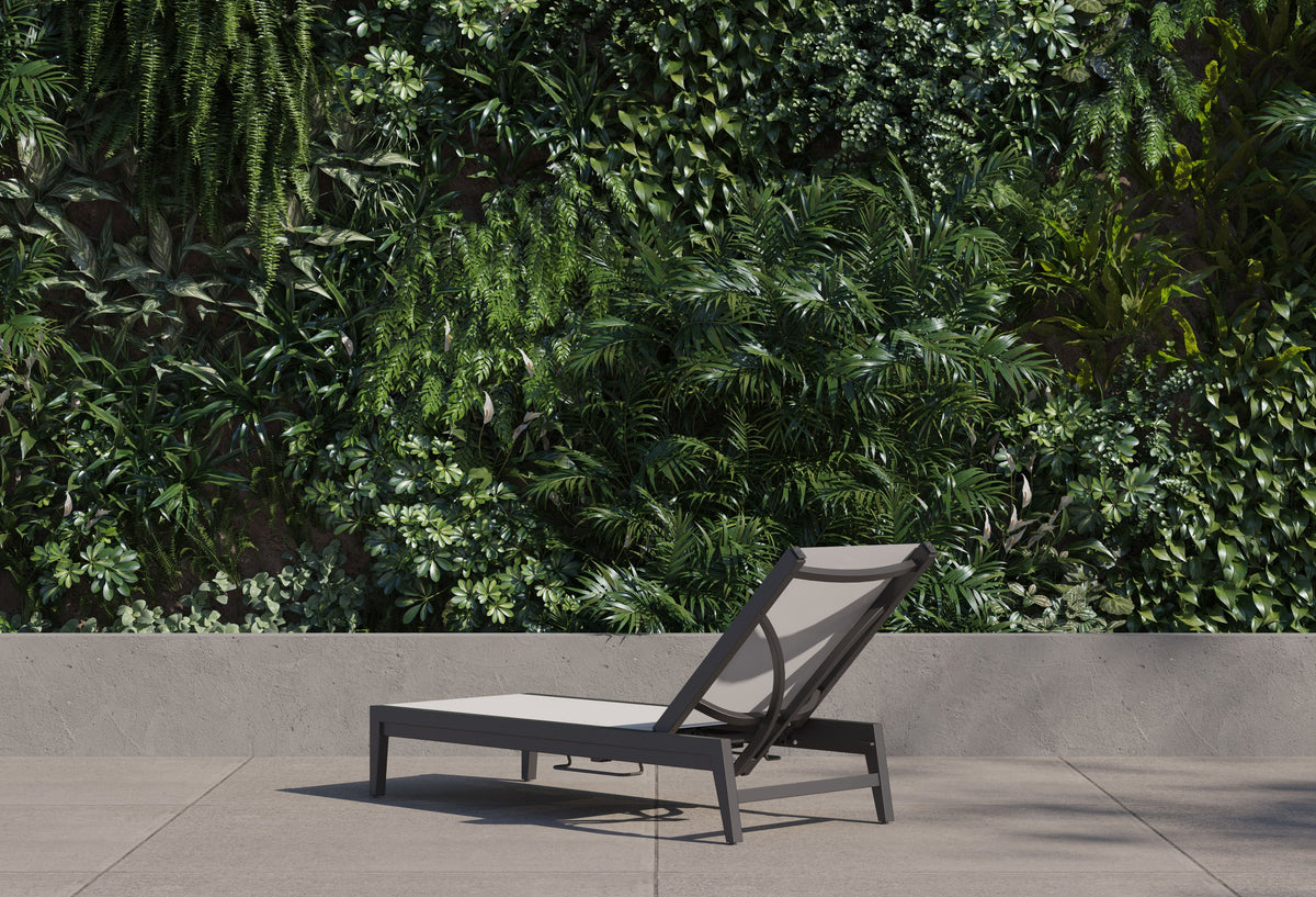 Aluminum outdoor chaise lounge with a sleek design, adjustable gray fabric sling, and reclining backrest, positioned against greenery.