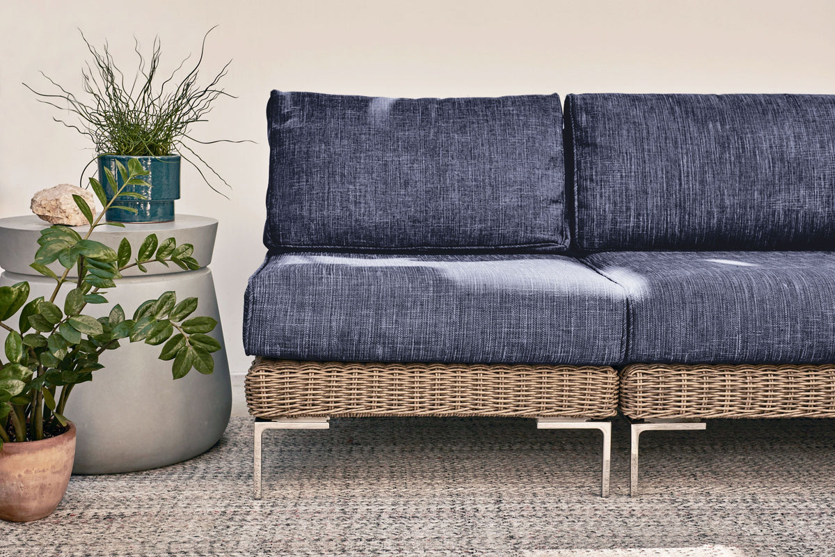 Handwoven brown wicker outdoor sofa with armless chairs, featuring layered navy cushions and stainless steel legs.