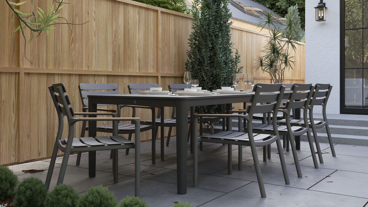 Rectangular outdoor dining table in Glacier White with eight gray armless chairs, set against a wooden fence.