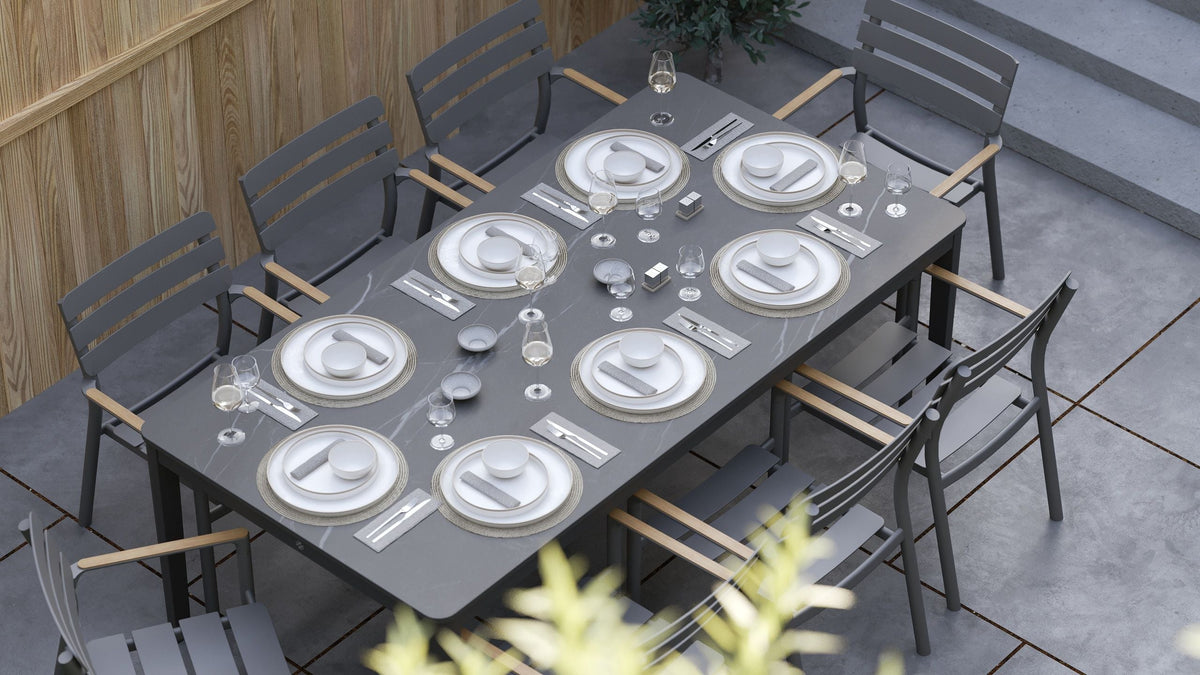 Rectangular OuterStone® dining table with a marbled gray surface, surrounded by eight sleek gray armless chairs with wooden accents.