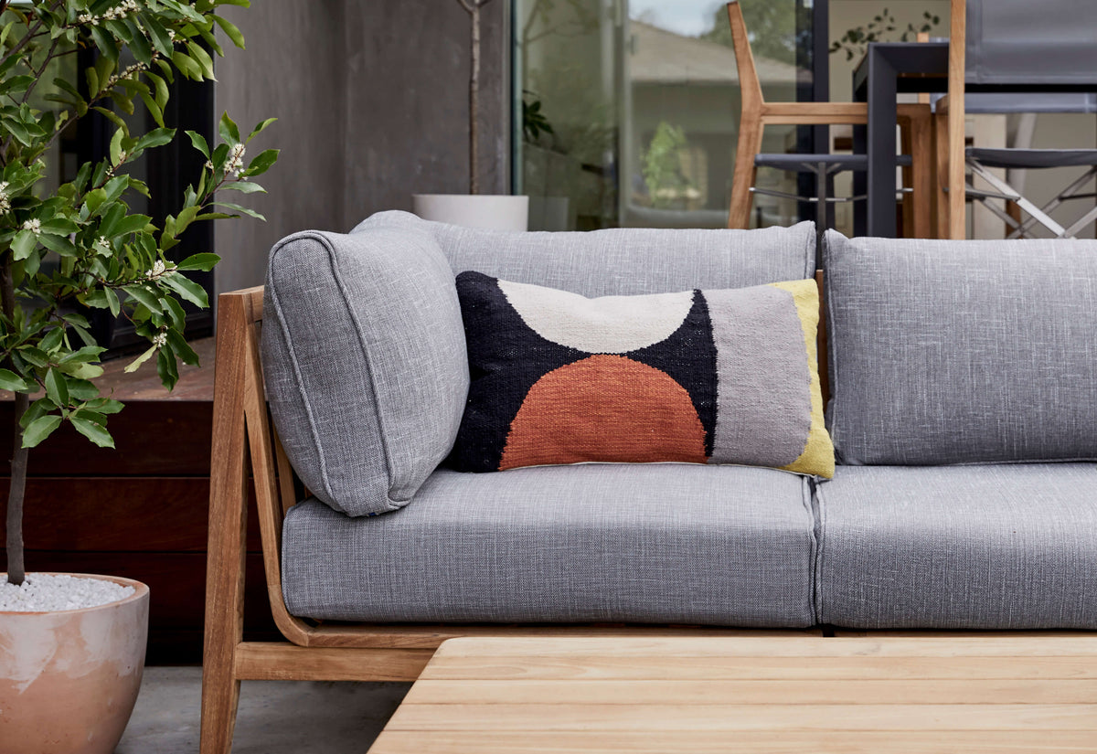 Teak outdoor U sectional seating in gray with a colorful geometric accent pillow, complemented by a wooden table.