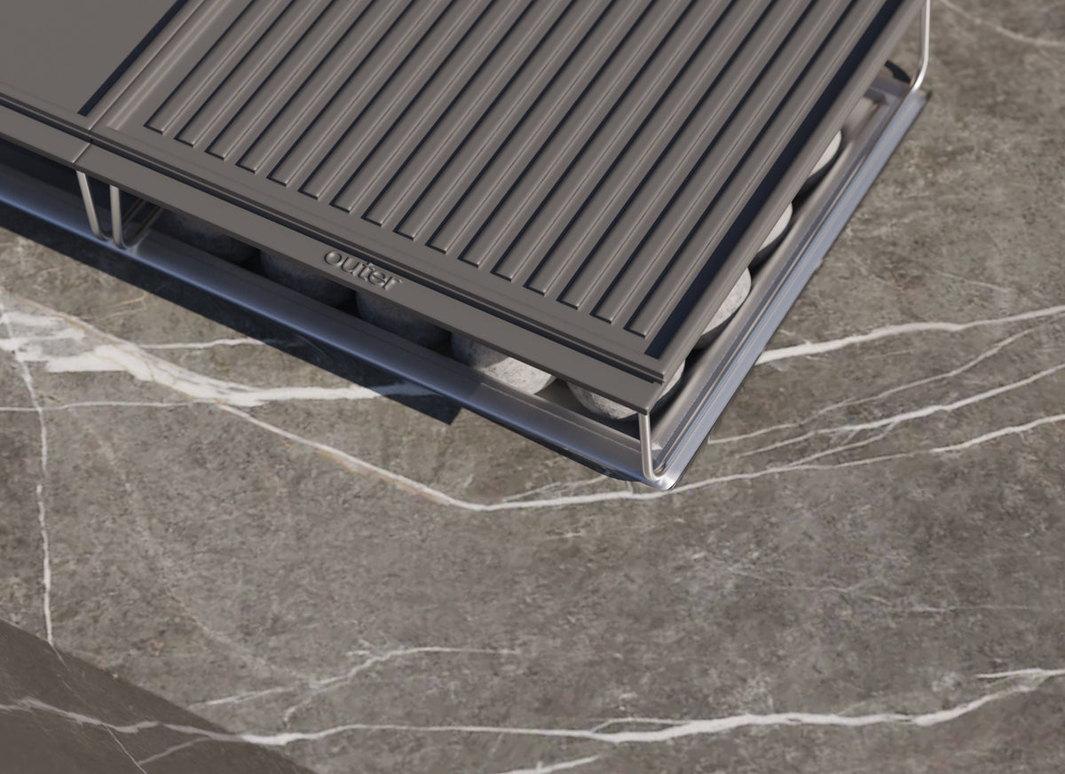 Rectangular OuterStone® fire pit cooking set with a stone surface, metal griddles, and ceramic fire spheres for outdoor use.