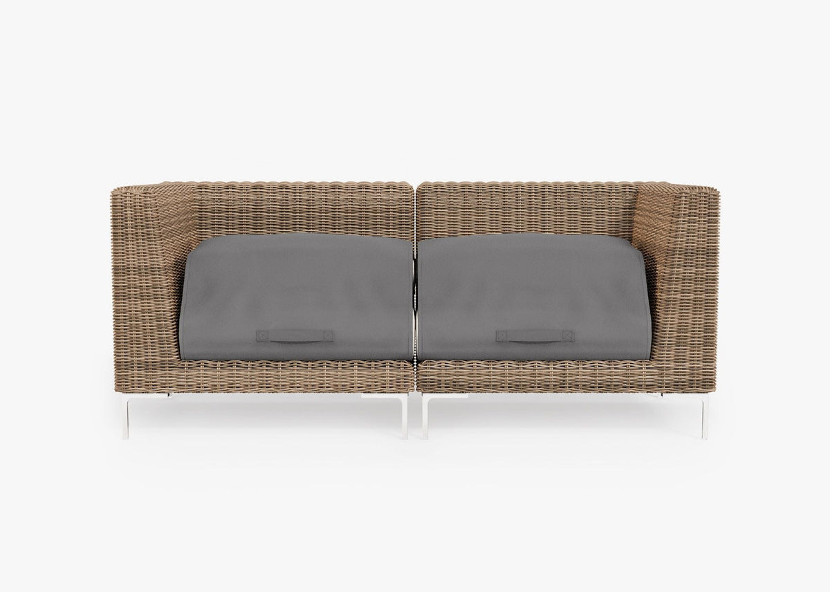 Handwoven brown wicker loveseat with polished stainless steel legs, featuring gray cushion covers for protection.