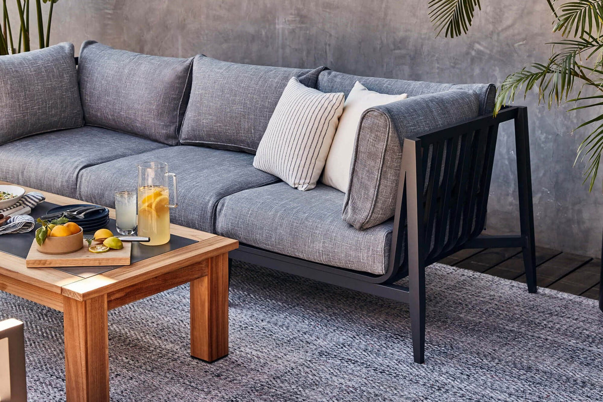 Charcoal aluminum U-shaped sectional with layered gray cushions and two accent pillows, shown with a wooden coffee table.