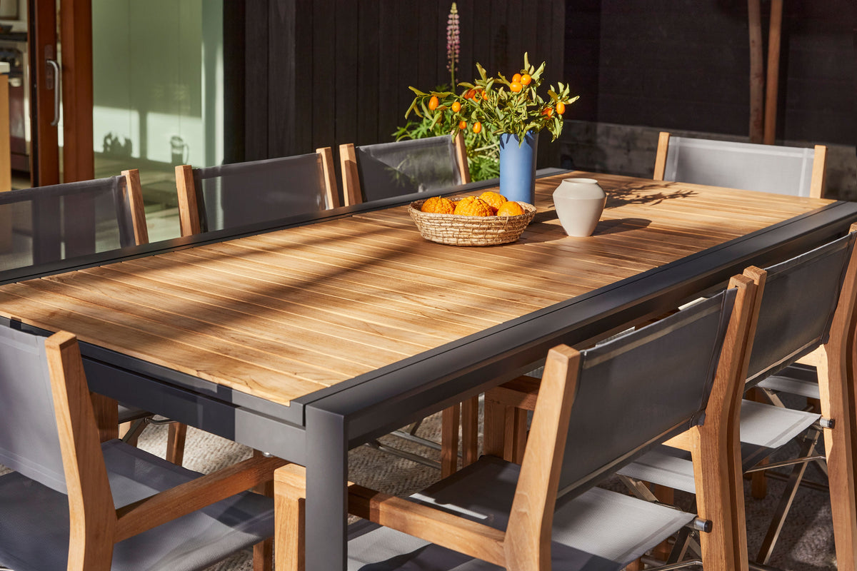Extendable dining table with a teak top and aluminum frame, surrounded by 12 folding teak director's chairs.