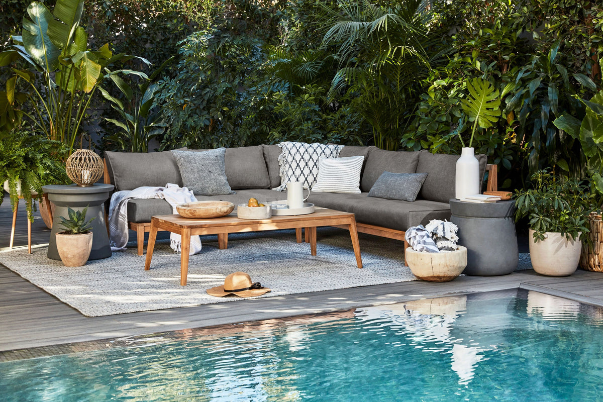 Teak Outdoor U Sectional – 7 Seat in gray fabric with five armless and two sectional chairs, set by a pool amid greenery.