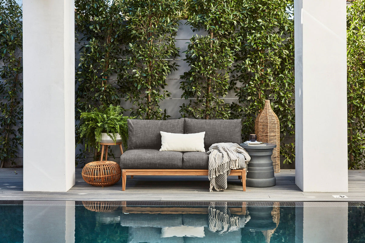 Gray upholstered U-shaped sectional sofa with wood frame, placed by the pool, with a white accent pillow and blanket.