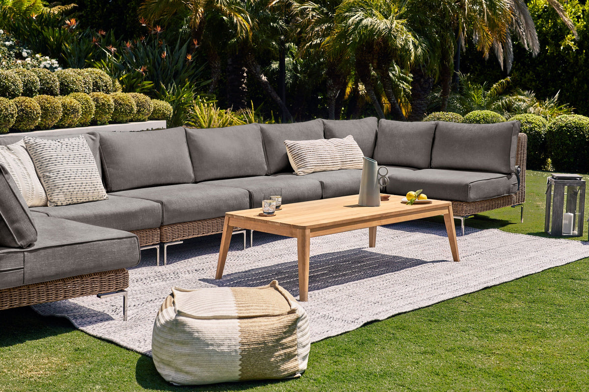 Handwoven brown wicker outdoor sofa with gray cushions, featuring a modular design, alongside a wooden coffee table.