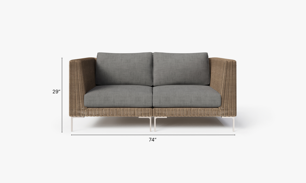 Handwoven brown wicker loveseat with gray cushions, featuring polished stainless steel legs, modular design, and outdoor durability.