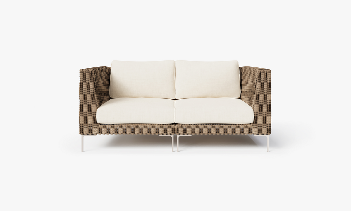 Handwoven brown wicker loveseat with cream cushions and polished stainless steel legs, designed for outdoor seating.