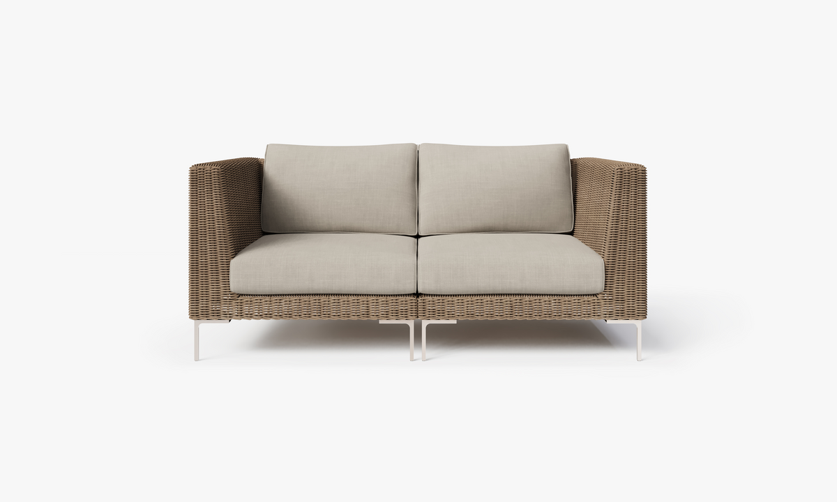 Handwoven brown wicker loveseat with plush beige cushions, polished stainless steel legs, and a modular design for flexible seating.