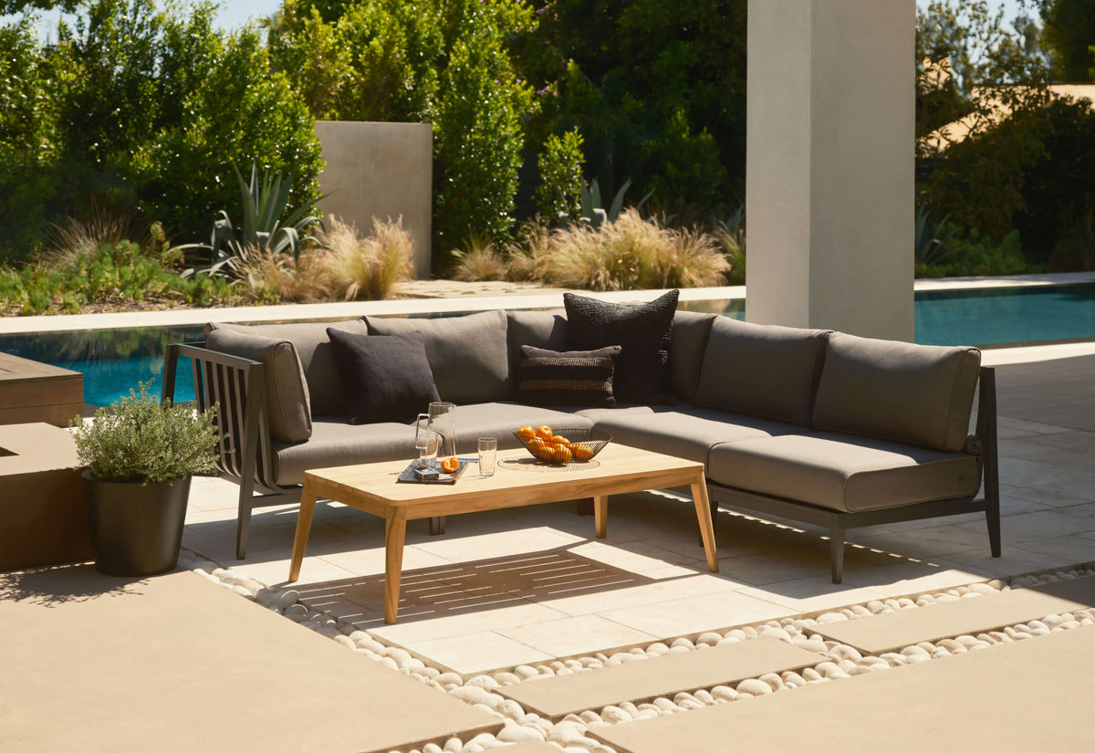 Charcoal aluminum L-shaped outdoor sectional with plush gray cushions, paired with a wooden coffee table and decorative accents.