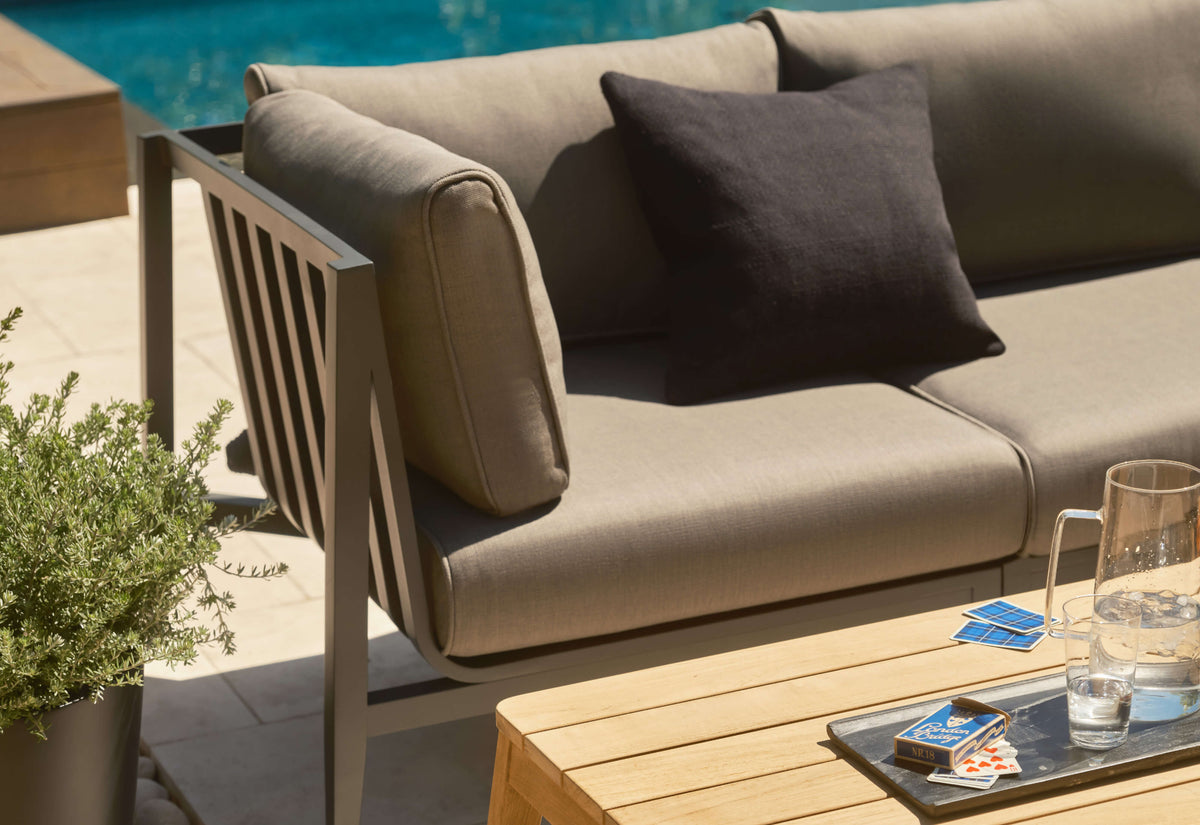 Charcoal aluminum three-seat outdoor sofa with light gray cushions, accented by a black throw pillow.