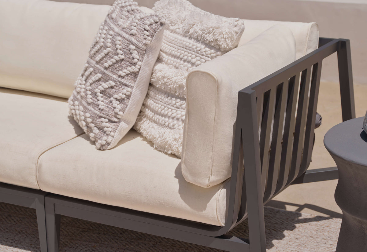 Charcoal aluminum L-shaped sectional with layered cream cushions and textured decorative pillows on one end.