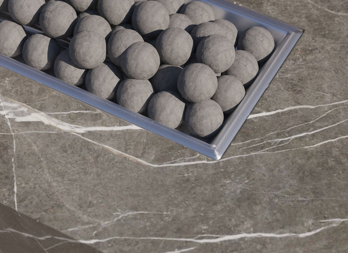 Gray ceramic fire spheres arranged in a rectangular metal tray on a sintered stone tabletop with subtle veining.
