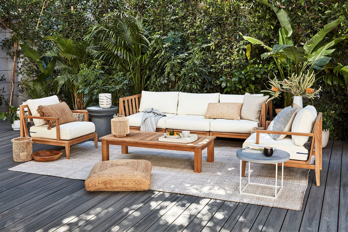 Teak outdoor U-shaped sectional with cream cushions, complemented by a natural wood coffee table and decorative pillows.